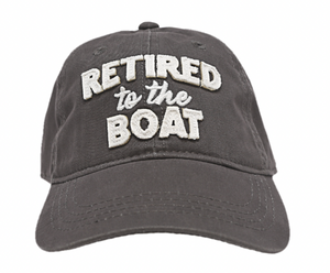 A dark gray baseball cap with "RETIRED to the BOAT" embroidered in bold, raised white letters on the front, highlighting a leisurely nautical lifestyle.