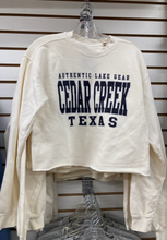 Load image into Gallery viewer, A close-up of a hanging ivory-colored fleece crew sweatshirt with &#39;AUTHENTIC LAKE GEAR CEDAR CREEK TEXAS&#39; printed in navy blue, displayed against a wooden slatwall background.