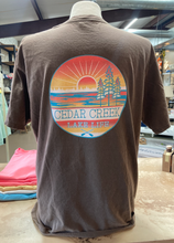 Load image into Gallery viewer, Back view of a coffee bean-colored tee with a large Cedar Creek Lake Life logo, displayed in a store.