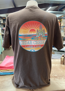 Back view of a coffee bean-colored tee with a large Cedar Creek Lake Life logo, displayed in a store.