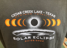 Load image into Gallery viewer, Close-up of a dark gray t-shirt featuring an intricate solar eclipse design with the moon covering the sun, accompanied by text &#39;CEDAR CREEK LAKE - TEXAS MAXIMUM TOTALITY SOLAR ECLIPSE 04/08/2024&#39;.