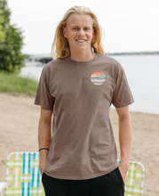 Load image into Gallery viewer, A  person by the lake wearing a coffee bean-colored tee with a small Cedar Creek Lake Life logo on the front.