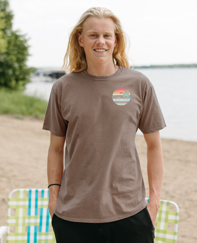 A  person by the lake wearing a coffee bean-colored tee with a small Cedar Creek Lake Life logo on the front.