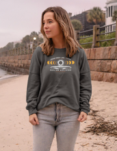 Load image into Gallery viewer, A young woman stands on a beachside walkway, wearing the Cedar Creek Lake Eclipse fleece crewneck in a relaxed fit, evoking the spirit of anticipation for the solar eclipse event.