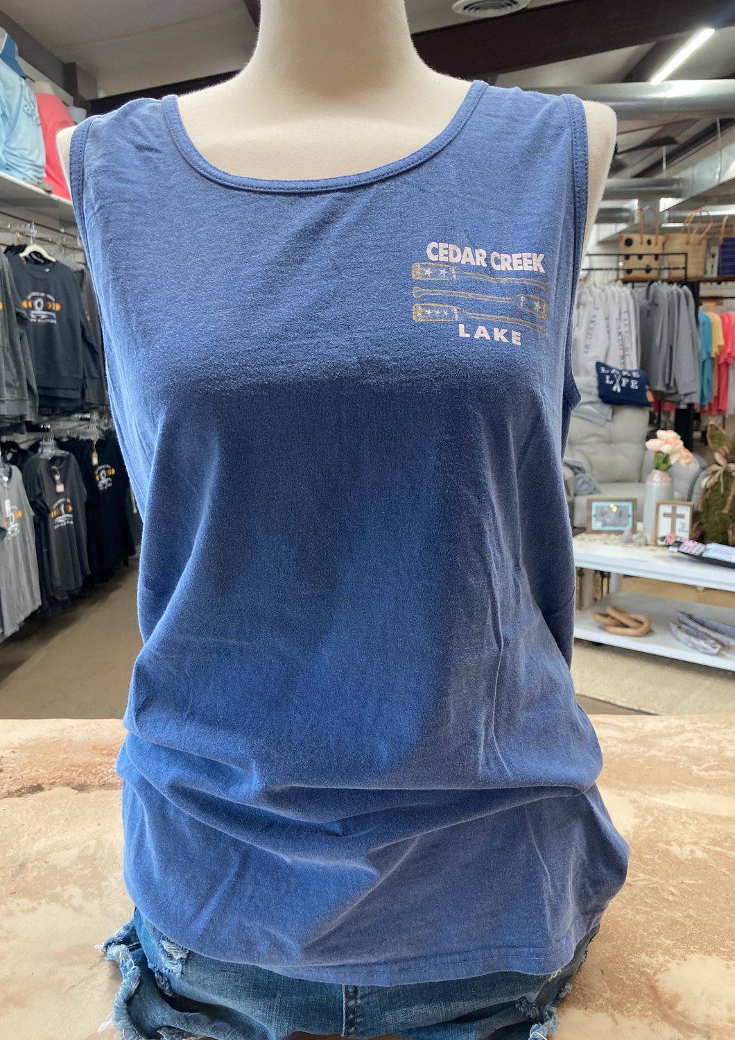 Casual pacific blue ringspun cotton tank top with 'Cedar Creek Lake' printed on the front, displayed on a mannequin in a boutique setting.