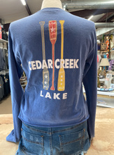 Load image into Gallery viewer, The back of a navy blue cropped ringspun cotton tee, featuring a vertical graphic of three paddles painted in red, white, and yellow with star details, placed above the words &#39;CEDAR CREEK LAKE&#39; in white block letters.