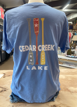 Load image into Gallery viewer, A cornflower blue ringspun cotton t-shirt displayed on a mannequin, showcasing the back design with three colorful paddles and the &#39;CEDAR CREEK LAKE&#39; print in bold white letters.