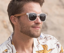 Load image into Gallery viewer, Man in patterned shirt smiling and wearing Blue Planet eco-friendly crystal-clear sunglasses with zebra wood arms and polarized lenses for stylish sun protection.