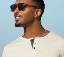 Load image into Gallery viewer, A confident man sporting taupe square-framed sunglasses with dark lenses, paired with a casual white henley shirt, embodies effortless style and summer vibes against a clear blue sky.
