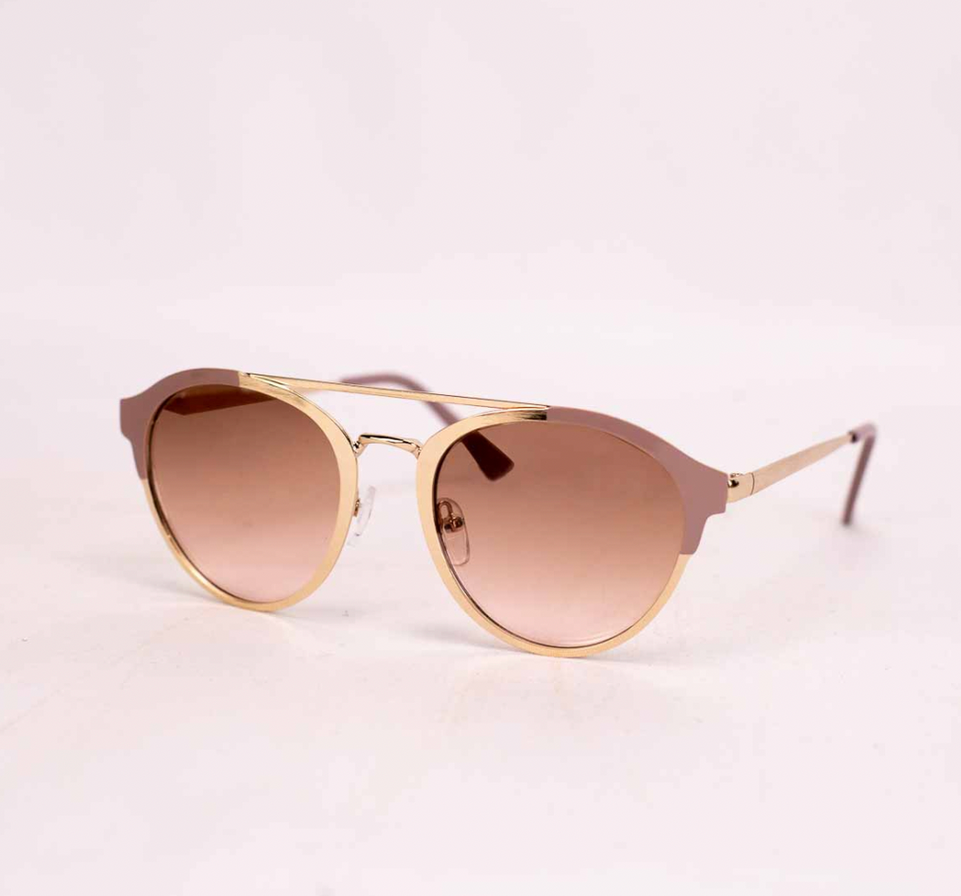 Elegant gold-framed sunglasses with a unique, semi-rimless design, featuring large round lenses that have a smooth, blush-tinted gradient. The frame has a distinctive, angular contour along the top edge, adding a modern twist to the classic round shape. The sunglasses rest against a soft beige background, highlighting their sophisticated and stylish design.