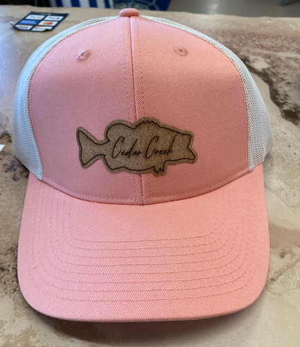 A coral-pink trucker hat featuring a distinctive bass-shaped cork patch with the words 