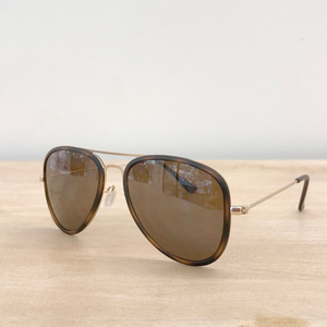 Elegant pilot-style sunglasses with olive green acetate frames and gold metal accents. The round lenses are shaded in a gradient dark tint. These glasses sit on a textured, neutral-toned surface, evoking a sense of classic style with a contemporary edge.